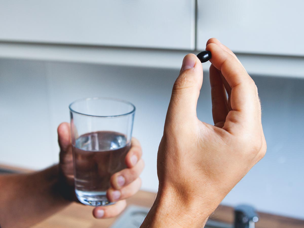 Two hands holding a glass of water and a CBD capsule.
