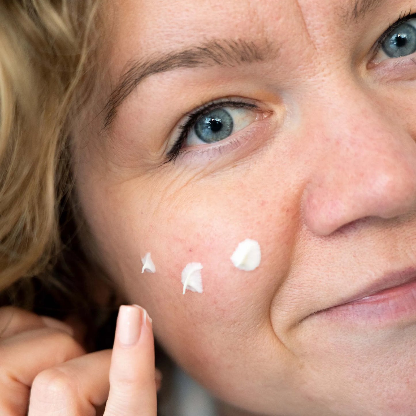 a woman spreads the cream on her cheek