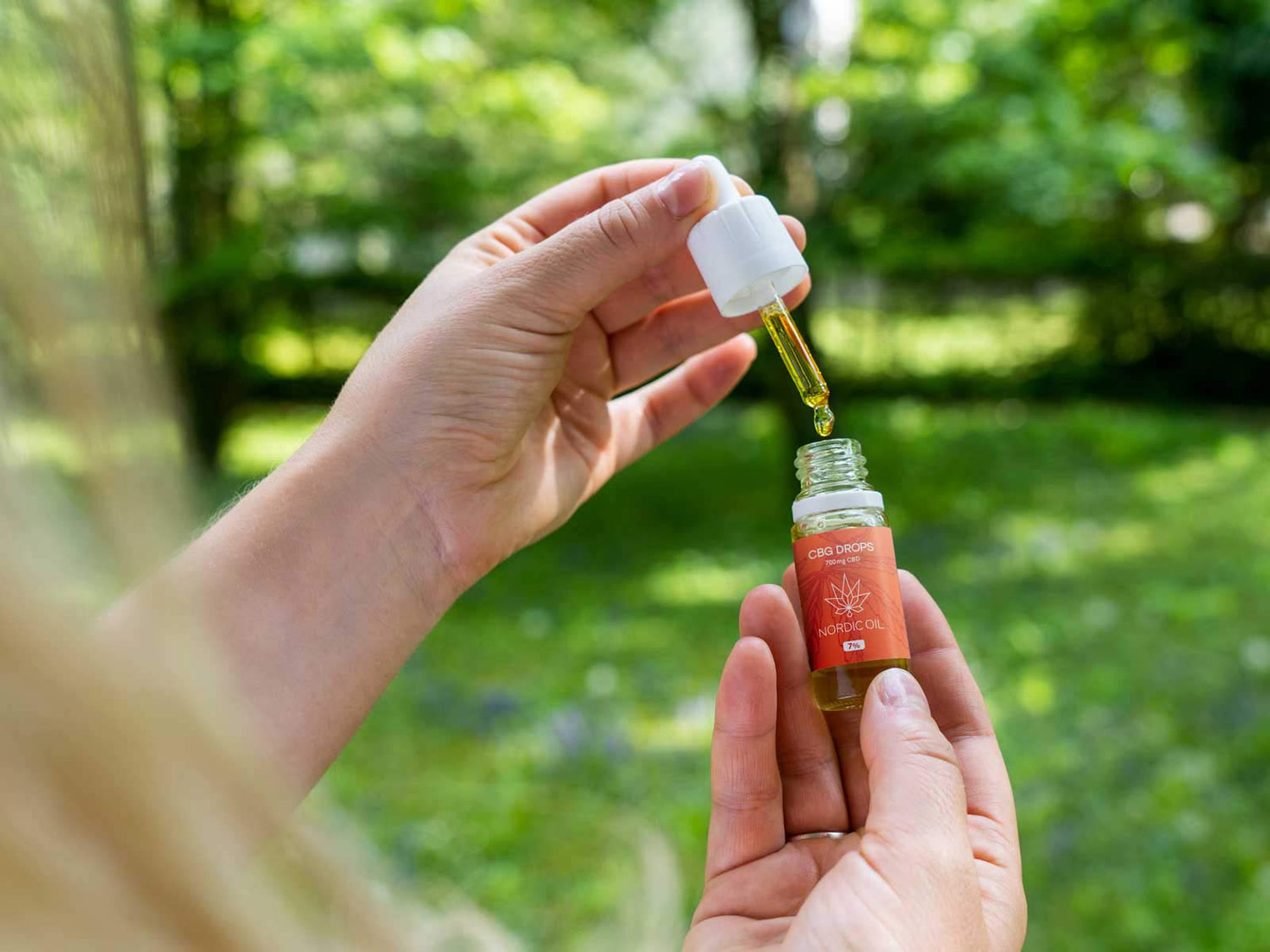 A woman holding an opened bottle and a pipette of 7% CBG Oil