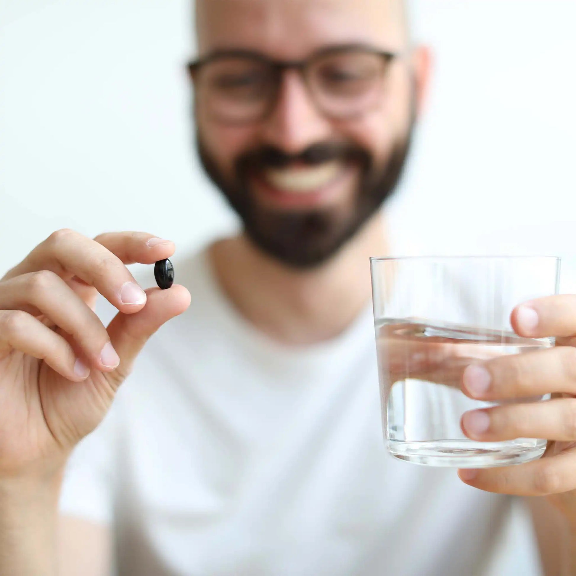 a customer holds a glass of water and a soft gelatine capsule in his hands