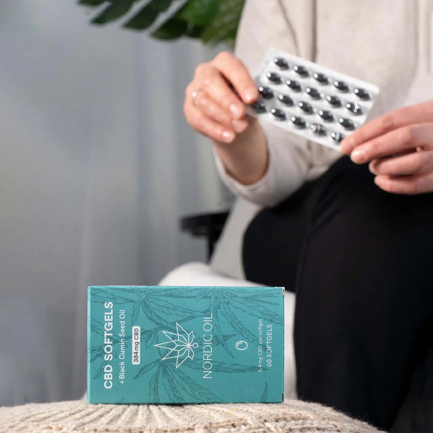 In the foreground, the package of CBD capsules; in the background, the customer holds the capsules.