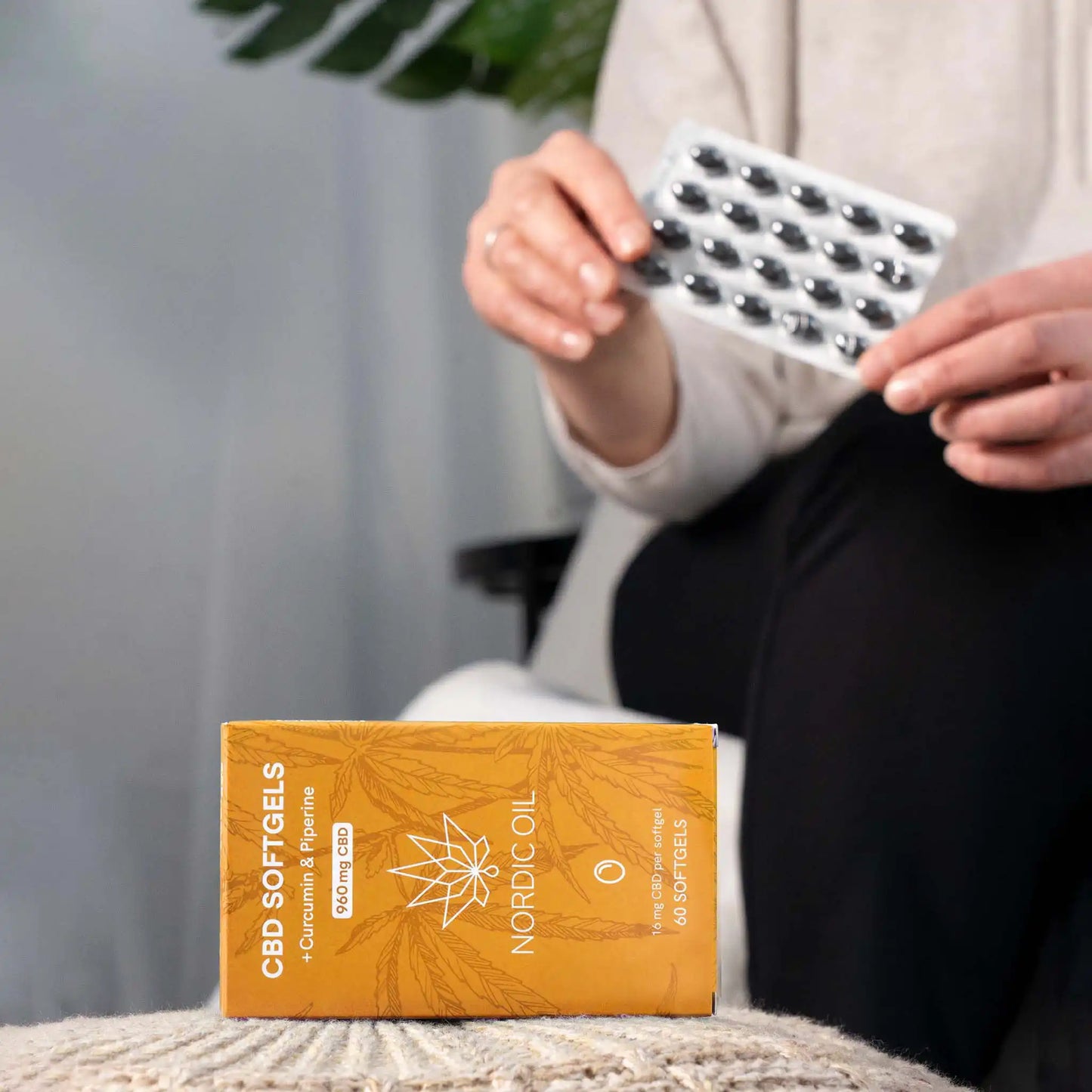 In the foreground, the package of CBD capsules; in the background, the customer holds the capsules.